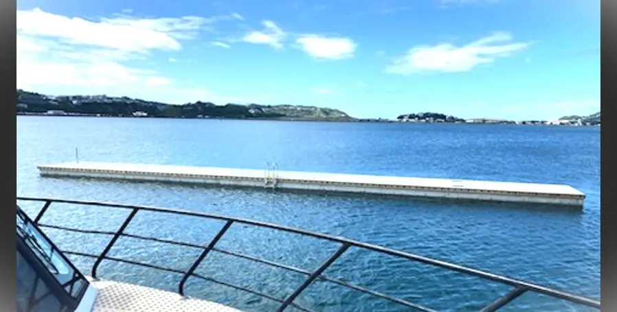 View from a boat showing a long floating dock on calm blue water with distant hills and a partly cloudy sky in the background.